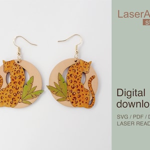 Puede incluir: Un par de pendientes de madera cortados con láser que presentan un diseño de leopardo con hojas verdes. Los pendientes son redondos y tienen un gancho dorado. El texto "LaserArtist studio" y "Descarga digital SVG / PDF / DXF ARCHIVOS LISTOS PARA LÁSER" es visible en la imagen.