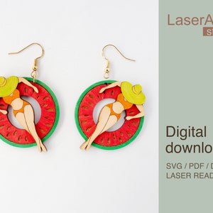 May include: A pair of laser cut wooden earrings featuring a woman in a swimsuit and sun hat relaxing on a watermelon-shaped float. The earrings are a bright red, green, and yellow.