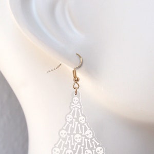 May include: White acrylic dangle earrings shaped like a Christmas tree with a skull and crossbones design.