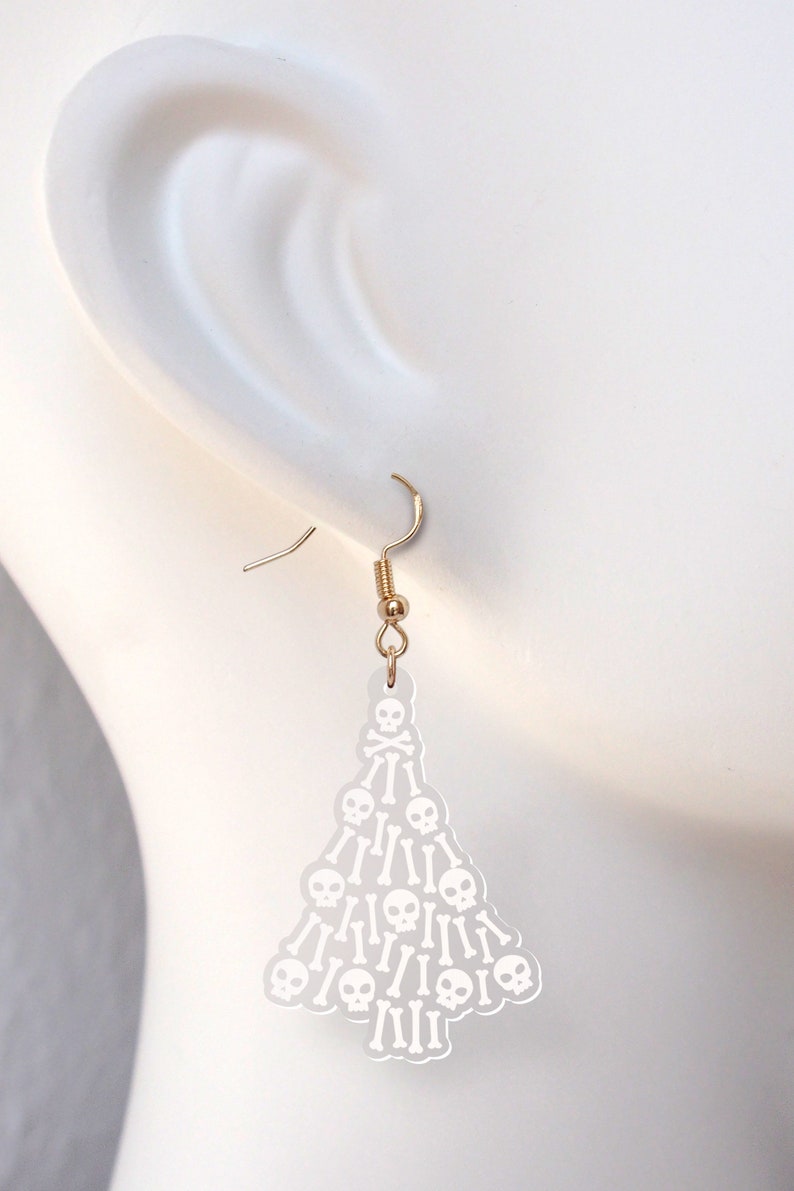 May include: White acrylic dangle earrings shaped like a Christmas tree with a skull and crossbones design.