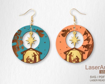 Op de afbeelding: Een paar lasergesneden houten oorbellen met een kerststal met een ster, engelen en een kribbe. De oorbellen zijn verkrijgbaar in twee kleuren: turquoise en koraal.