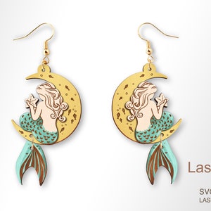 May include: A pair of wooden earrings featuring a mermaid sitting on a crescent moon with a starfish. The mermaid has long blonde hair and a teal tail. The earrings are laser cut and ready to be assembled.