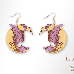 May include: A pair of wooden dragon earrings. Each earring features a dragon design with purple wings and accents, set against a light brown crescent moon shape. The earrings have gold-colored hooks. The LaserArtist studio logo is visible.