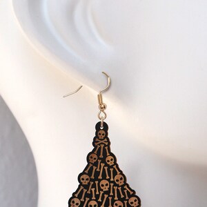 May include: A pair of wooden earrings shaped like a Christmas tree, decorated with black skulls and crossbones.