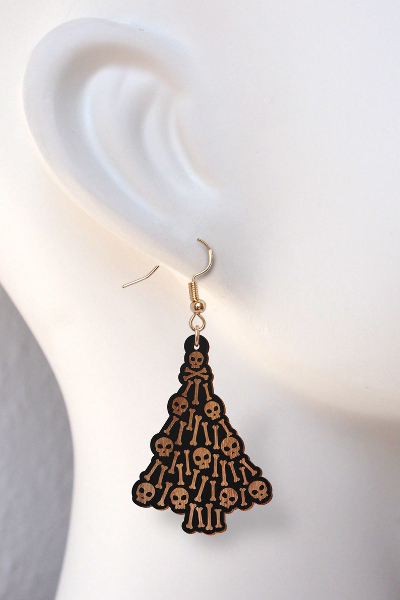 May include: A pair of wooden earrings shaped like a Christmas tree, decorated with black skulls and crossbones.