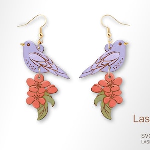 May include: A pair of laser cut earrings featuring a purple bird with a pink flower cluster hanging below. The earrings are made of wood and have a gold hook.
