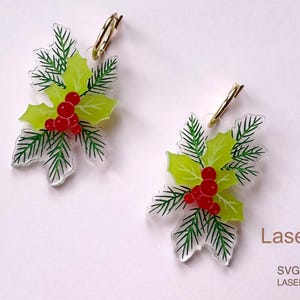 Puede incluir: Un par de pendientes festivos con un diseño de hojas de acebo. Cada pendiente tiene un cierre dorado, hojas verde claro, agujas de pino verde oscuro y bayas rojas. Un accesorio de temporada.