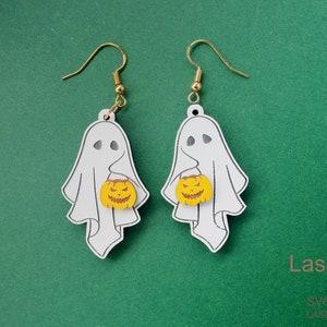 Puede incluir: Un par de pendientes con temática de Halloween. Cada pendiente presenta un fantasma blanco sosteniendo una calabaza amarilla. Los pendientes tienen ganchos dorados. El fondo es de color verde liso.