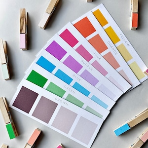 May include: A set of color swatches with the names of each color printed on the cards: brown, green, blue, purple, pink, orange, yellow. The cards are arranged in a fan shape and are held together with clothespins.