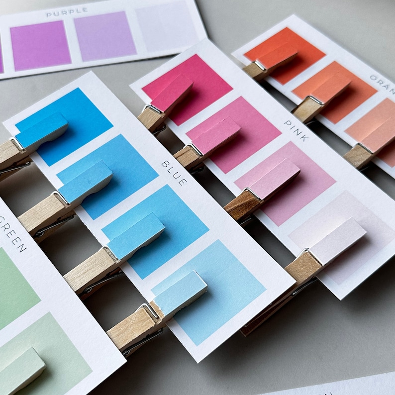 May include: A set of color swatches with labels for purple, green, blue, pink, and orange. The swatches are attached to the cards with clothespins.