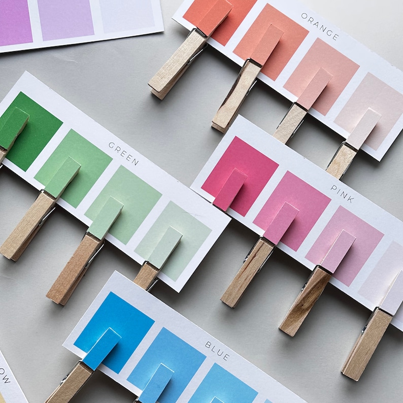 May include: Five color cards with different shades of blue, green, pink, orange, and red. Each card has the color name printed on it and is attached to a wooden clothespin.