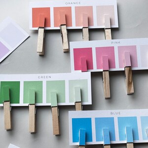 May include: A set of color swatches with wooden clothespins. The swatches are labeled "Orange", "Pink", "Green", and "Blue".