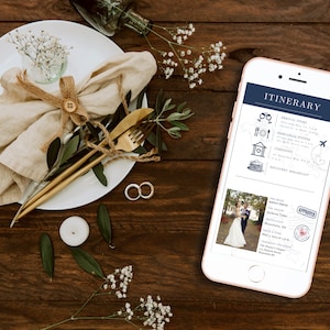 May include: A smartphone displaying a wedding itinerary with a blue and white color scheme. The itinerary includes details for the arrival night, rehearsal dinner, ceremony, and a discovery breakfast. The phone is on a wooden table with a white plate, a napkin, and a gold fork and knife.