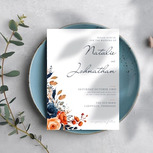 Puede incluir: Invitación de boda con los nombres "Natalie y Johnathan" en escritura cursiva. La invitación incluye la fecha, hora y lugar: The Old Barn, Caryville, Tennessee. Acentos florales en azul marino, naranja y marrón adornan la esquina inferior izquierda.