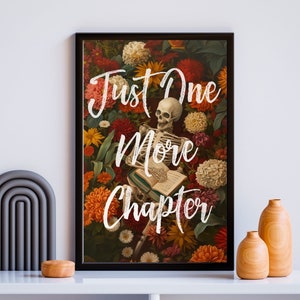 May include: A black framed print with a skeleton reading a book surrounded by colorful flowers. The text "Just One More Chapter" is written in white on the print.