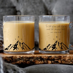 Könnte beinhalten: Zwei durchsichtige Glasbecher mit schwarzen Berg- und Sternmotiven. Der Becher rechts trägt den Text "To the stars who listen and the dreams that are answered".