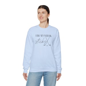 May include: A light blue sweatshirt with the text "I like men with big sticks" in black script. Two crossed hockey sticks are below the text. The sweatshirt is worn by a person.
