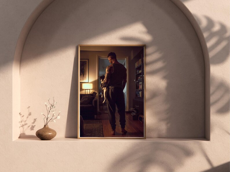 May include: A framed photograph of a person holding a small animal, likely a pet. The photograph is displayed on a shelf with a vase and decorative plant. The room is dimly lit with warm tones.