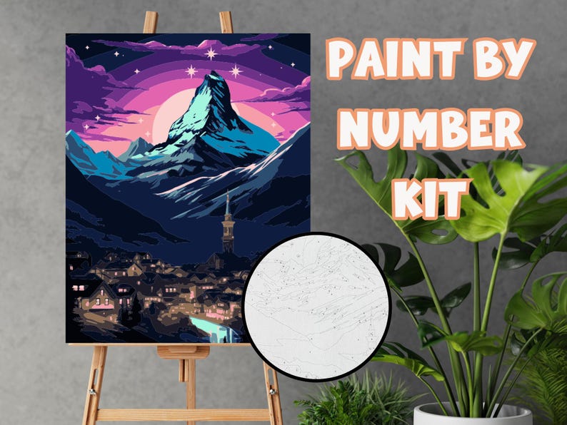 K&ouml;nnte beinhalten: Ein Malen-nach-Zahlen-Set mit einer Berglandschaft und einem Dorf am Fu&szlig;e. Das Kunstwerk zeigt einen Berg unter einem rosa-violetten Himmel, mit dem Text "PAINT BY NUMBER KIT" auf der rechten Seite.