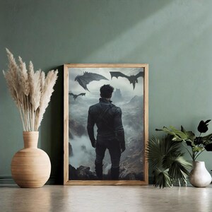 May include: A framed print of a man standing in a misty landscape with three black dragons flying overhead. The man is wearing a black leather jacket and jeans. The print is in a wooden frame.