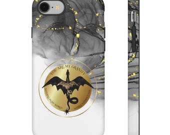 May include: A phone case with a black, white, and gold marble design. The case features a gold circle with a dragon illustration and the text "YOU ARE MY GRAVITY, NOTHING IN MY WORLD WORKS WITHOUT YOU."