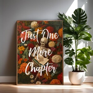 May include: A framed print with a skeleton laying on a book surrounded by colorful flowers. The text "Just One More Chapter" is written in white on the print.