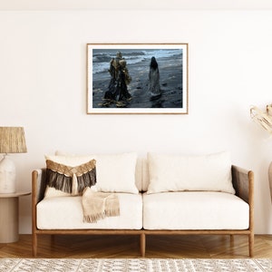 May include: A framed photograph of two figures in long flowing robes walking on a beach. The figures are silhouetted against a stormy sky and the ocean waves. The beach is dark and wet.