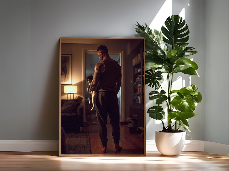 May include: A framed mirror reflects a person holding a small dog in a well-lit room. A large potted plant with green leaves stands beside the mirror. The room has a warm, inviting atmosphere with a wooden floor.