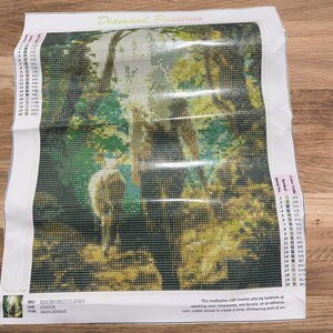 May include: A diamond painting kit featuring a forest scene with a deer. The image is composed of small, colorful squares, creating a mosaic effect. The kit includes a canvas, color codes, and instructions.
