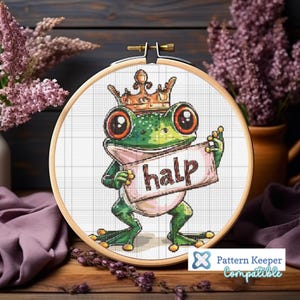 May include: A green frog wearing a gold crown holds a pink sign that says "halp". The frog is in a white embroidery hoop.