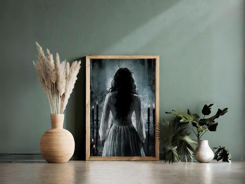 May include: A framed print of a woman in a white dress standing in a dark, shadowy room. The woman's back is to the viewer, and she has long, dark hair. There are candles on either side of her.