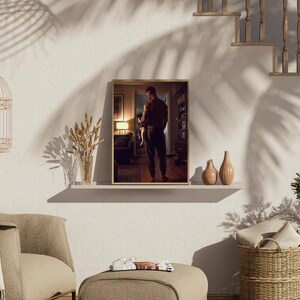 May include: A framed print of a person holding a small dog, displayed on a white shelf with two decorative vases. The room is decorated with a birdcage, a chair, and a footstool. The image is lit by natural light, with shadows from a nearby plant.