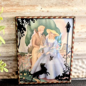May include: A framed vintage print featuring a couple in a garden setting, with a black silhouette of a dog. The woman wears a blue dress and yellow hat. The frame has a red and brown striped border.