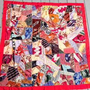May include: A handmade patchwork quilt with a vibrant mix of patterned fabrics in various colors, including red, blue, and brown. The quilt is framed with a solid red border.