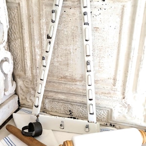 May include: White metal kitchen rack with a distressed finish, alongside a white rolling pin with wooden handles and a wooden rolling pin. A black metal ring is also present. The items rest on a white and blue striped cloth.