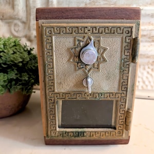 May include: A vintage-style mailbox with a bronze finish and a wooden top. The mailbox features an ornate design with a combination lock and a small window. The overall aesthetic is reminiscent of antique postal boxes.