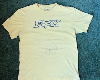 May include: A yellow t-shirt with a blue Fox Racing logo. The logo features the word "FOX" in a bold font with a fox head in the middle.