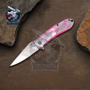 Pu&ograve; includere: Un coltello tascabile pieghevole con una lama argentata e un manico rosa. Il manico presenta un disegno a farfalla. Il coltello &egrave; prodotto da Wolfsmith.
