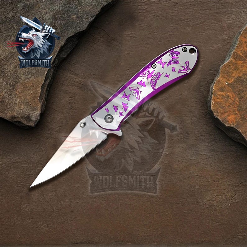 Pu&ograve; includere: Un coltello pieghevole argentato con una lama lucida e un manico con un design a farfalle viola. Il coltello ha un logo Wolfsmith nell'angolo in alto a sinistra.
