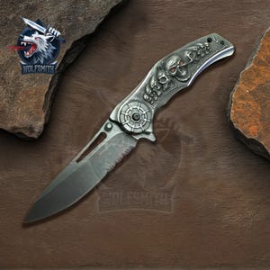 May include: A silver pocket knife with a skull and crossbones design on the handle. The blade is partially open and has a serrated edge.