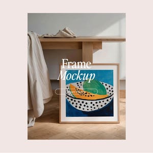 May include: A framed print of a painting depicting a bowl of fruit. The bowl is white with black polka dots and contains a papaya and a lime. The background of the painting is blue. The frame is light brown wood.