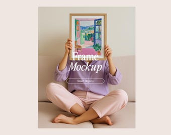 Op de afbeelding: Een ingelijst kunstwerk met een kleurrijke landschapsafbeelding wordt voor het gezicht van een persoon gehouden. De lijst is lichtbruin. De persoon draagt een paars overhemd en een roze broek. De tekst "Frame Mockup" is zichtbaar.