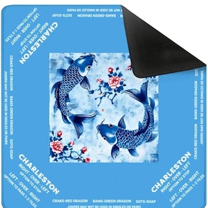 以下が含まれることがあります： 2 匹の鯉のイラストが描かれた青と白のゲームマット。マットには花のアクセントと「Charleston」の文字とゲームの説明があります。マットは角が丸い長方形です。