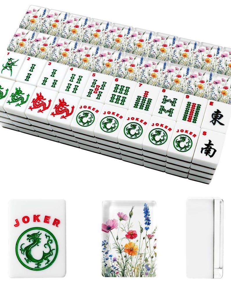 May include: A set of white Mahjong tiles with black markings and colorful floral accents. The tiles feature Chinese characters, dragons, and the word "JOKER". The set includes tiles with numbers and suits.