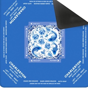 May include: A blue and white Charleston game mat with a decorative floral and fish design. The mat includes text indicating game play instructions and the names of the game pieces. The mat is rectangular.