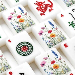 以下が含まれることがあります： 赤色の龍、ピンクやオレンジ、青色の野花が描かれた花柄、緑と赤の円形モチーフ、黒色の漢字と赤色の数字が刻まれた、白色の長方形の麻雀牌のセット。それぞれの牌には異なるデザインが施されており、整然と並べられている。