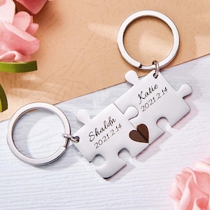 May include: Two silver puzzle piece keychains with the names "Shaldn" and "Katie" engraved on them, along with the date "2021.2.14". The pieces fit together to form a heart.