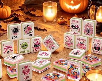 May include: A collection of rectangular mahjong tiles featuring various colorful illustrations including cats, dragons, flowers, and text such as SOAP, GREEN, RED, and JOKER. The tiles have white faces with pink and green edges, arranged in a scattered display.