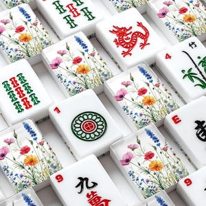 May include: White Mahjong tiles with colorful floral designs and red, green, and black symbols. The tiles feature numbers, Chinese characters, and suit symbols. The floral design includes pink, orange, and blue flowers.