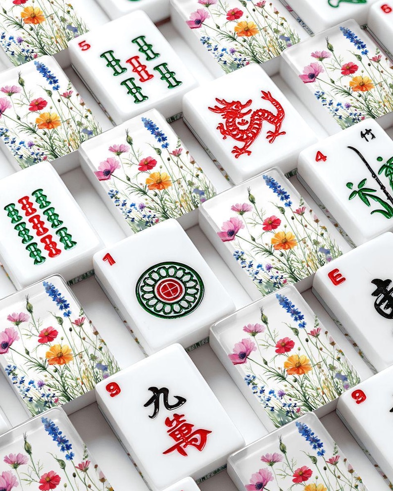 May include: White Mahjong tiles with colorful floral designs and red, green, and black symbols. The tiles feature numbers, Chinese characters, and suit symbols. The floral design includes pink, orange, and blue flowers.